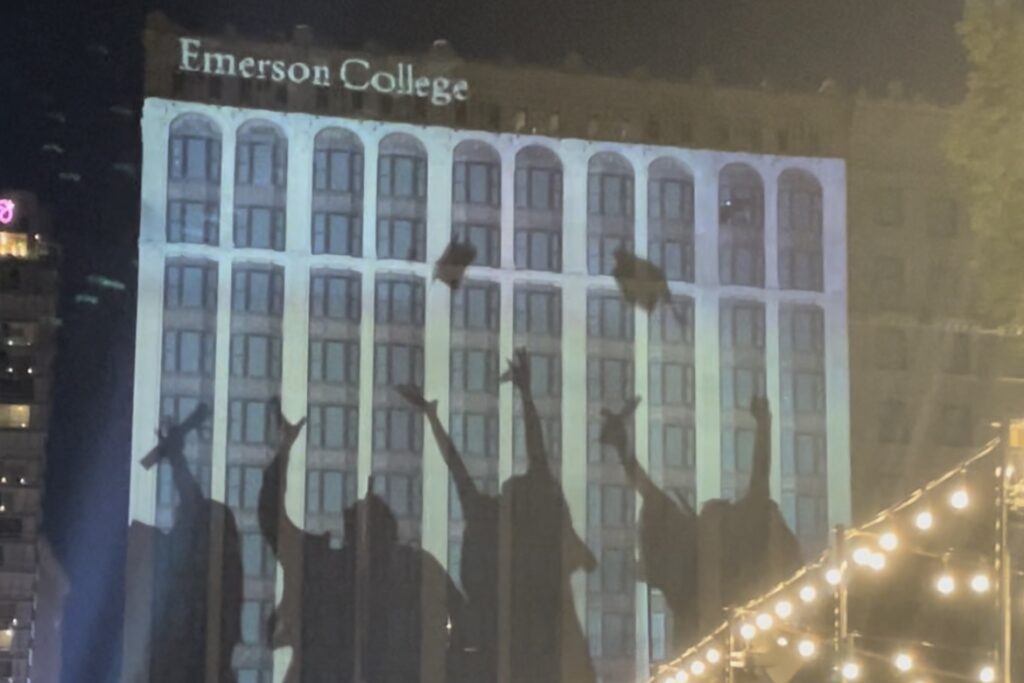 A projection on a building facade of a group of graduates throwing their caps into the air.