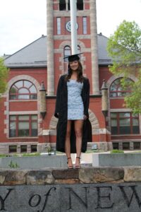 A student in her cap and down stands in front of a University of New Hampshire building.