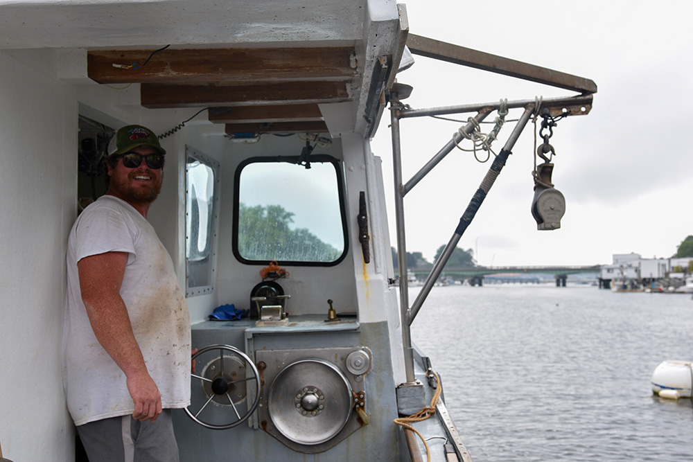 Chris Tobey smiles beyond the camera while standing at the wheel of his boat
